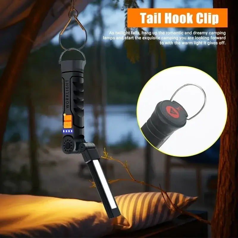 Portable LED work light with tail hook clip illuminating a camping scene, perfect for outdoor adventures.